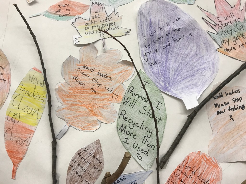 Photo of art created by Junior School students of leaves and flowers that have inspirational promises or requests, such as "I will try to pick up trash on the ground and throw it out" or "World leaders please stop cutting down trees."