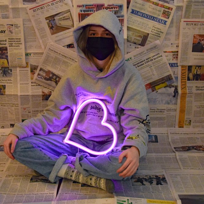 Photo of student holding neon heart around newspapers.