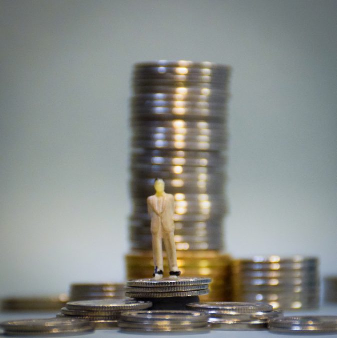 Image of a small figurine standing in front of a stack of coins.